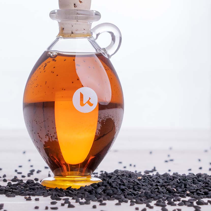 Pure, cold-pressed black seed oil in a hand-blown glass amphora with seeds